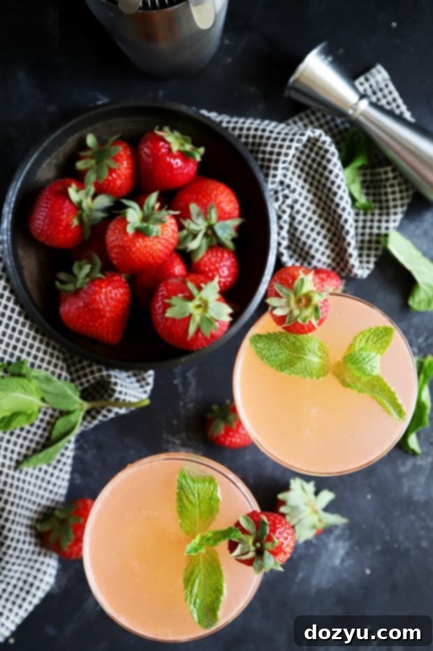 Minted Strawberry Vodka Gimlet 2 Overhead view of two Strawberry Mint Vodka Gimlets in coupe glasses, surrounded by fresh strawberries and mint leaves, evoking a perfect summer drink.
