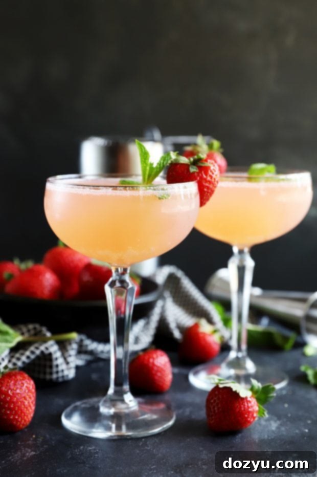 Minted Strawberry Vodka Gimlet 3 Close-up of a Strawberry Mint Vodka Gimlet in a coupe glass, garnished with fruit and herbs, with another glass in the background, perfect for a summer gathering.