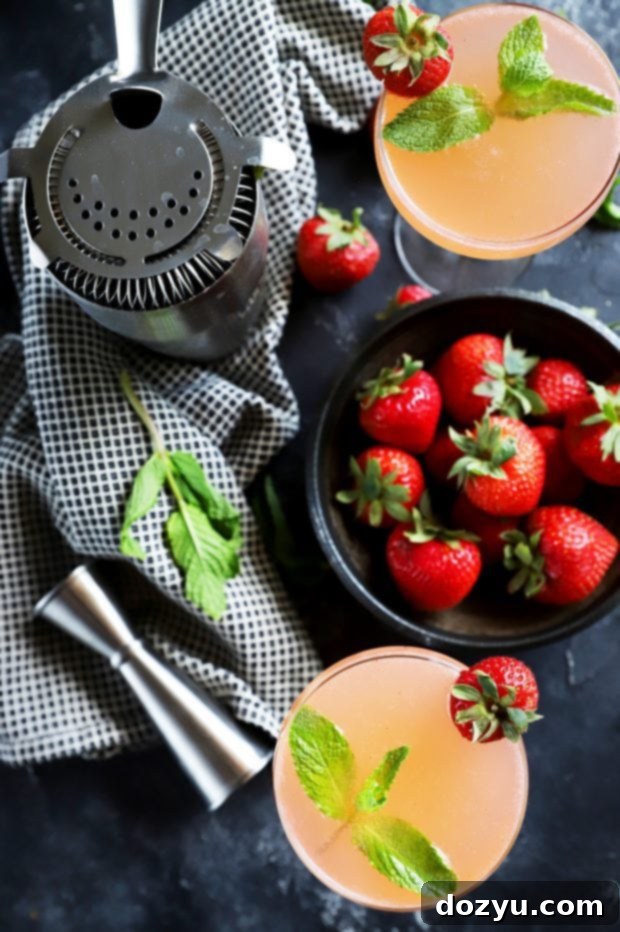 Overhead shot of two Strawberry Mint Vodka Gimlets, surrounded by fresh berries and mint sprigs on a rustic surface, highlighting its refreshing appeal.