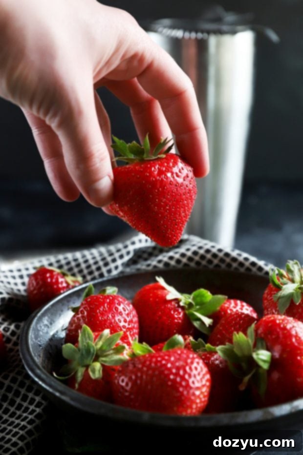 Minted Strawberry Vodka Gimlet 6 A hand reaching into a bowl of fresh, ripe strawberries, highlighting the fresh ingredients used in the Strawberry Mint Vodka Gimlet.