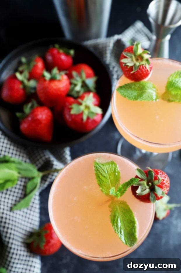 Minted Strawberry Vodka Gimlet 7 An array of fresh berries and mint leaves alongside vodka in a cocktail shaker, ready to be mixed into a refreshing gimlet, with two finished drinks in coupe glasses.