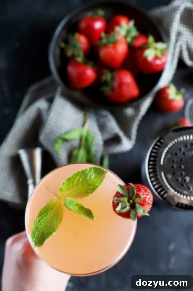 Minted Strawberry Vodka Gimlet 9 Close-up of a hand holding a Strawberry Mint Vodka Gimlet, emphasizing the refreshing nature of the drink in a summer setting.