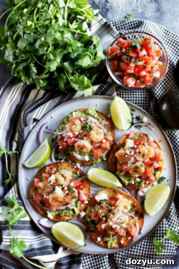 Overhead shot of honey lime shrimp and guacamole tostadas on a platter, garnished with limes and cilantro