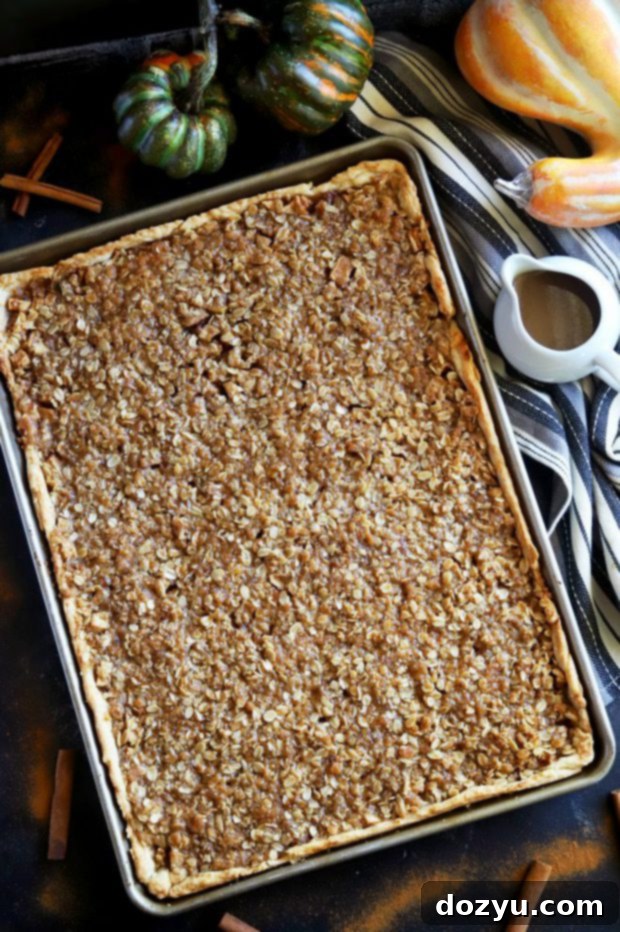 A large slab apple pie baking in a half sheet pan, with a golden crumb topping.
