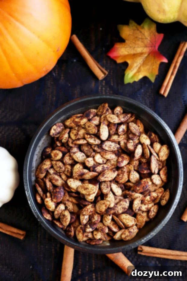 A medium-sized glass bowl filled with raw pumpkin seeds, glistening with a generous coating of seasoned melted butter and a medley of colorful spices, perfectly prepped for baking.