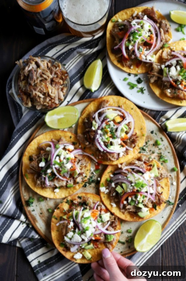 A hand reaching for a crispy pork carnitas tostada from a bountiful platter.