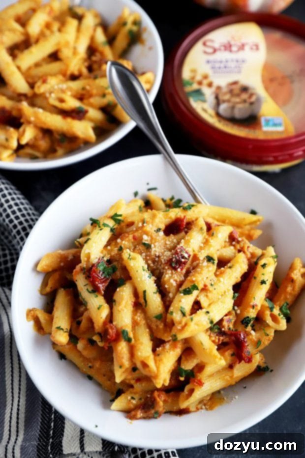 Garlic-Roasted Pumpkin Hummus Pasta 8 Fork lifting creamy pumpkin pasta from a bowl, showing the texture and sun-dried tomatoes.