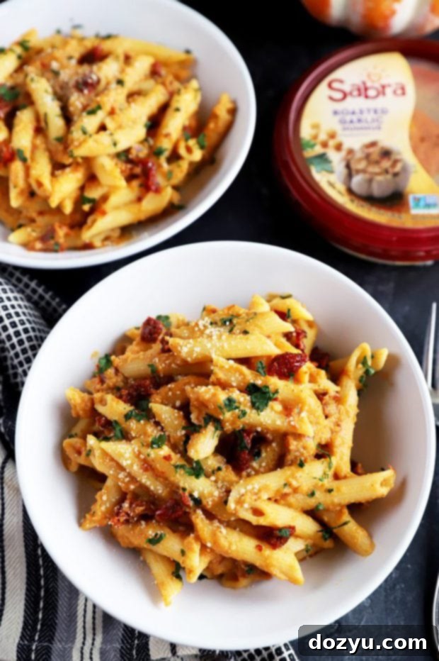 Garlic-Roasted Pumpkin Hummus Pasta 9 Bowl of creamy pasta with pumpkin and hummus, garnished with fresh herbs.