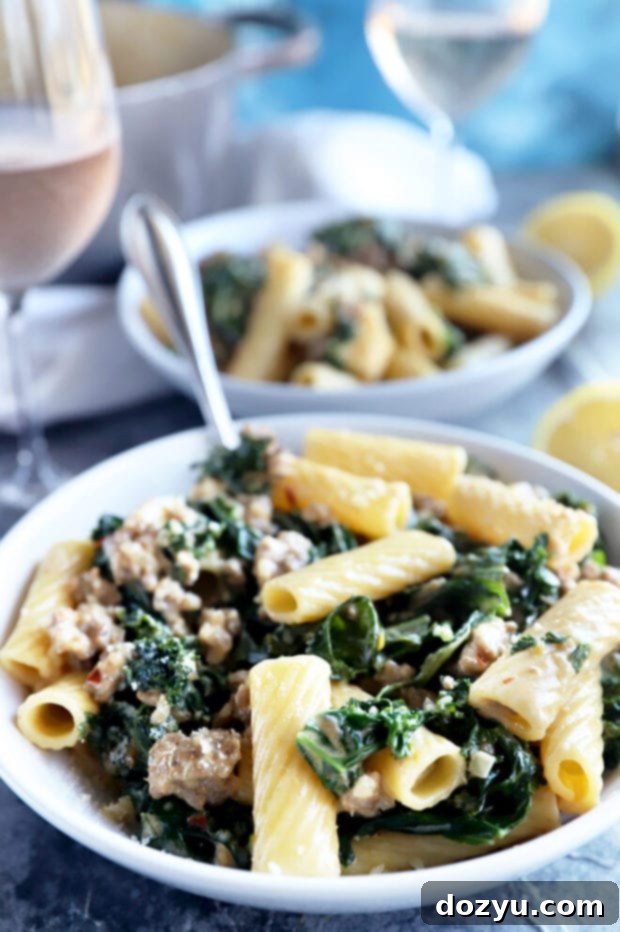Rich Creamy Sausage Kale Rigatoni 2 A bowl of creamy sausage kale rigatoni pasta, garnished with fresh herbs and a lemon wedge.