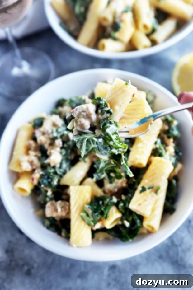 Rich Creamy Sausage Kale Rigatoni 6 A fork lifting creamy sausage kale rigatoni pasta from a bowl, highlighting the texture and ingredients.