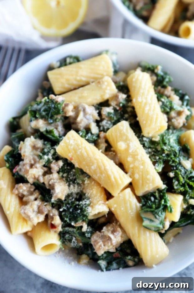 Rich Creamy Sausage Kale Rigatoni 8 A close-up of creamy sausage kale rigatoni pasta in a bowl, with a fork and a lemon wedge.