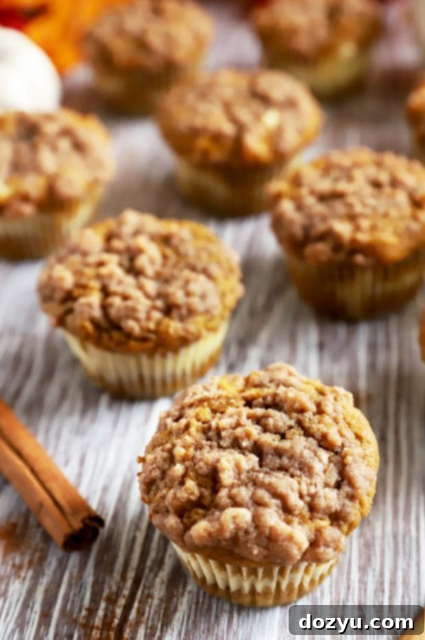 Cream Cheese Swirl Pumpkin Crumble Muffins 5 Side view of a stack of pumpkin cream cheese muffins on a wooden board, showcasing their golden tops and soft texture