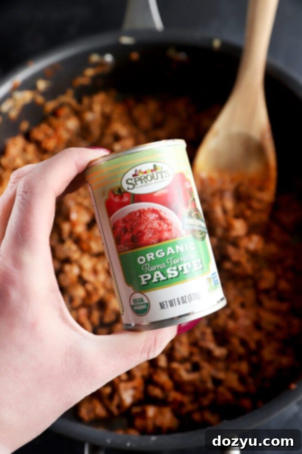 Savory Greek Beef Wraps 8 Hand holding a can of tomato paste, ready to add to the beef mixture