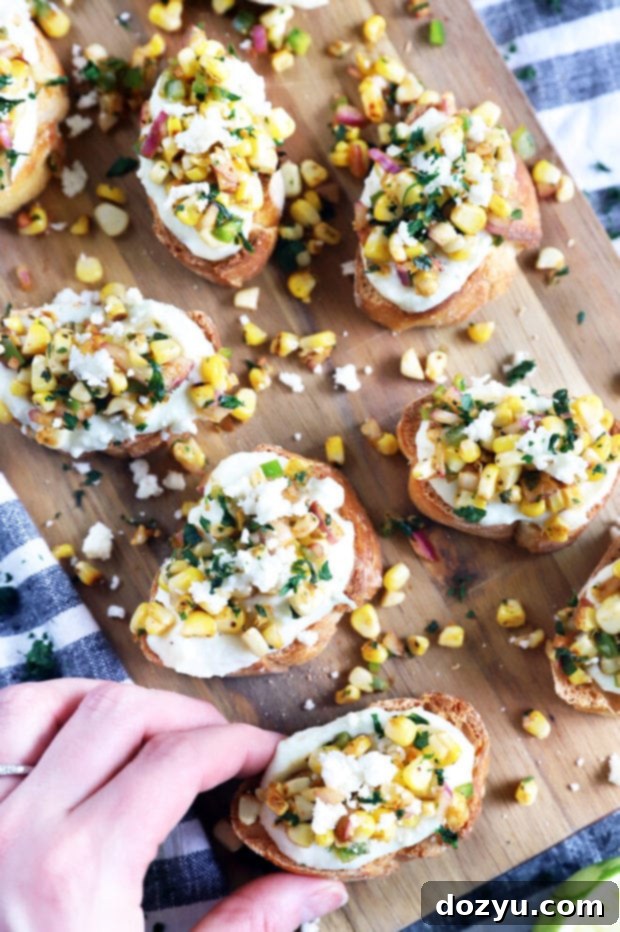 Zesty Grilled Elote Crostini 4 Overhead shot of a hand holding a single grilled mexican corn crostini