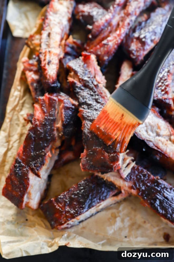 Fall-Off-The-Bone Apple Cider Traeger Ribs 9 brushing bbq sauce on pork sliced on parchment paper