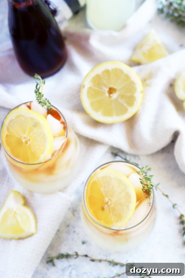 The Sparkling Arnold Palmer 5 Two glasses of sparkling Arnold Palmer, garnished with lemon and herbs, on a wooden table.