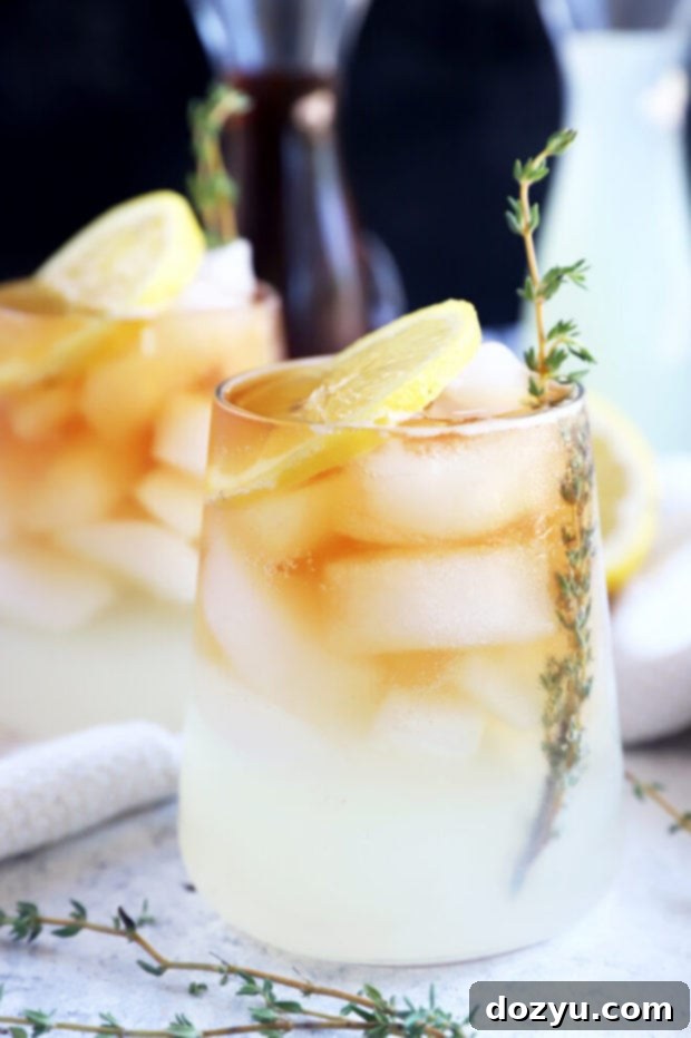The Sparkling Arnold Palmer 6 A close-up shot of a sparkling Arnold Palmer with a lemon slice and a sprig of thyme, showcasing its refreshing quality.