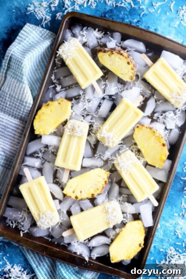 Tropical Pina Colada Popsicles 3 Overhead photo of Pina Colada Popsicles arranged beautifully on a sheet pan with ice, emphasizing their refreshing appeal