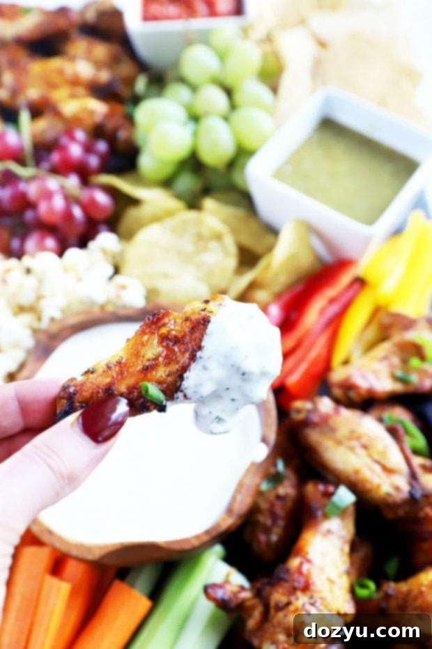 Epic Game Day Grazing Board 4 Close-up of a hand holding a grilled chicken wing dipped in a white sauce