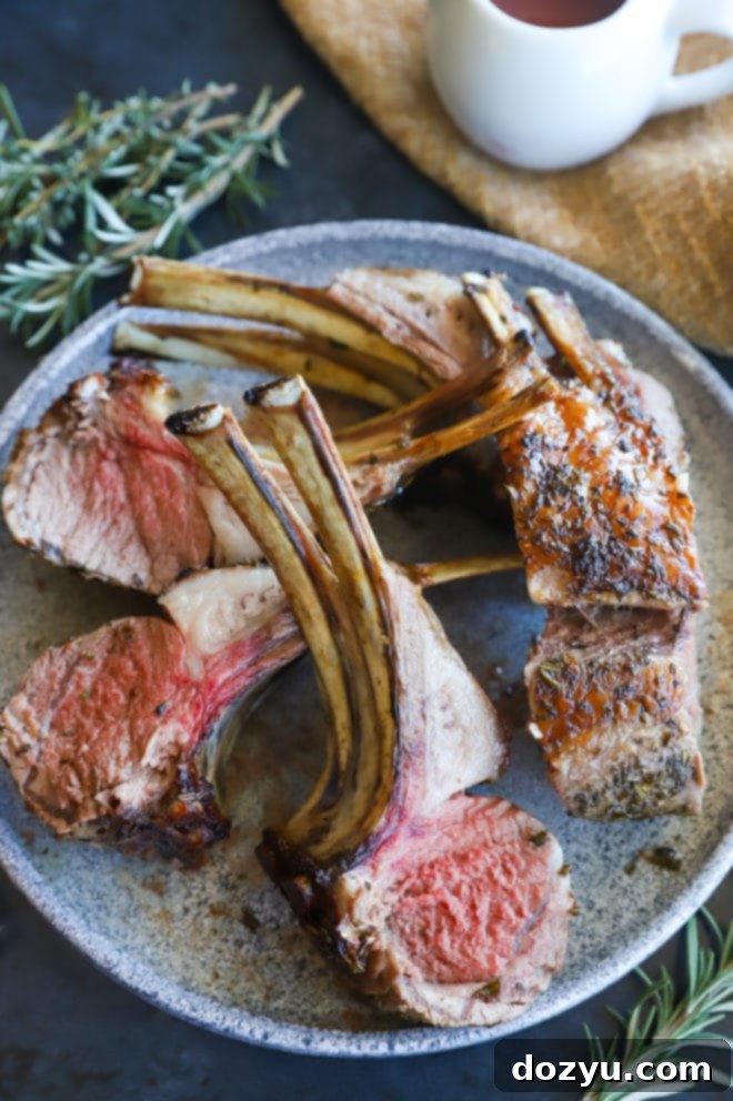 Tender Herb Crusted Lamb Rack with Robust Red Wine Sauce 6 A beautifully roasted Herb Crusted Rack of Lamb, sliced into individual chops, served on a white plate with a side of rich red wine sauce and fresh rosemary.