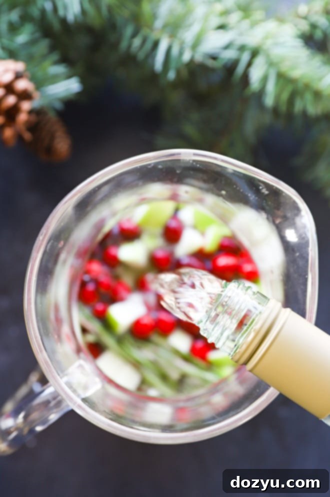 Merry & Bright Sangria 5 Pouring white wine into a glass pitcher filled with cranberries and apples for Christmas Sangria
