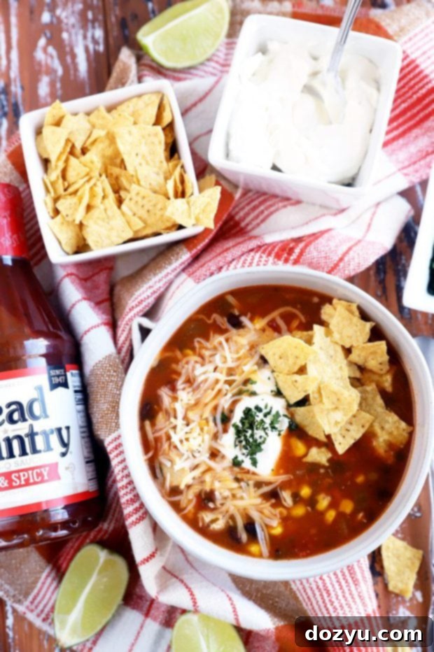 Smoky Instant Pot Turkey Enchilada Soup 5 A bottle of Head Country BBQ sauce proudly stands beside a bowl of the smoky turkey enchilada soup, emphasizing its role as a core ingredient.