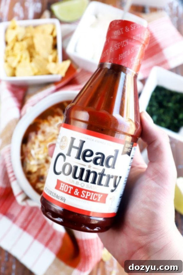 Smoky Instant Pot Turkey Enchilada Soup 6 A hand holding a bottle of Head Country Bar-B-Q sauce, ready to be added to a dish, emphasizing its quality and rich flavor profile.
