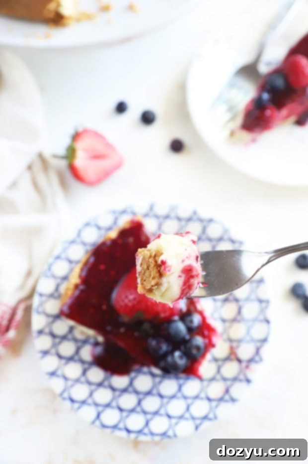 Berry Medley Cheesecake 5 A fork holding a perfect bite of Triple Berry Cheesecake, showing layers of crust, creamy filling, and berry topping.