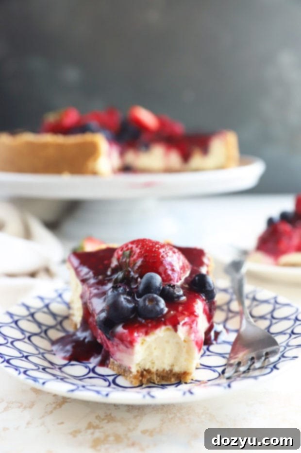 Berry Medley Cheesecake 7 A perfectly cut slice of Triple Berry Cheesecake with a fork resting beside it, ready to be enjoyed.