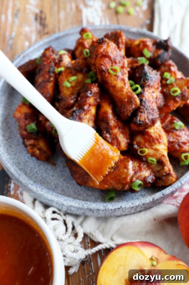 Sticky Bourbon Peach BBQ Wings 7 Close-up of a hand brushing bourbon peach BBQ sauce onto grilling chicken wings