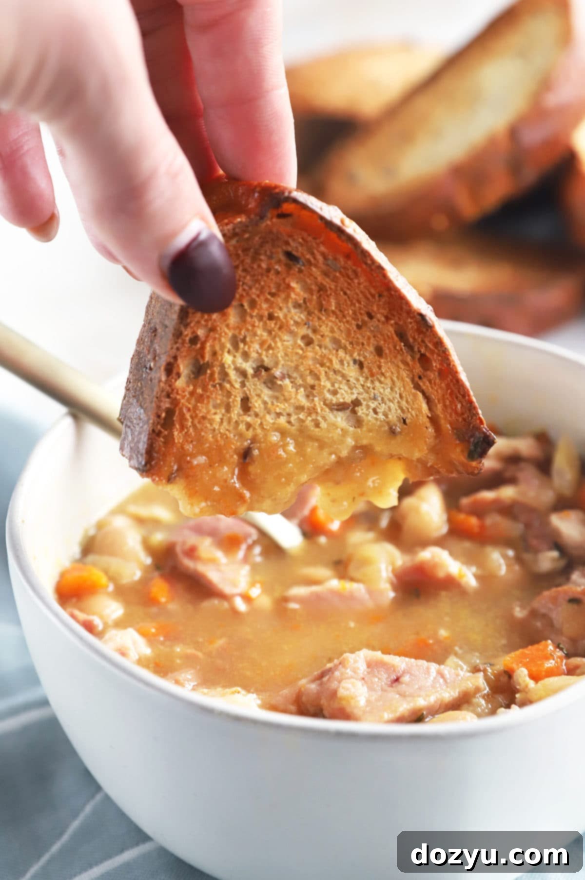 One Pot Ham and Bean Delight 7 Another perspective of a hand dipping bread into a bowl of Instant Pot Ham and Bean Soup, emphasizing the comforting nature of the meal.