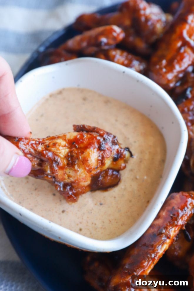 Glazed Honey BBQ Chicken Wings 8 Close-up picture of a grilled chicken wing being dipped into a creamy white sauce, emphasizing the deliciousness and the perfect pairing