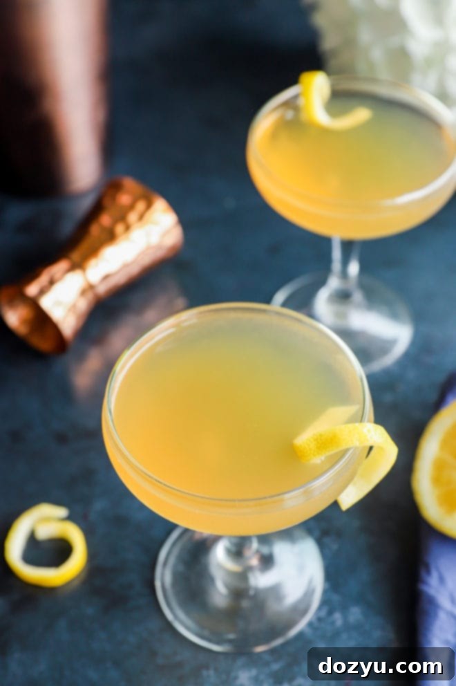 Overhead view of two Sidecar cocktails in glasses, garnished with lemon twists, beside whole and sliced lemons.