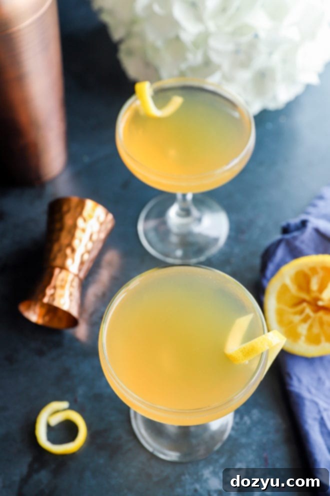 A Bourbon Sidecar cocktail with whole lemons and floral garnishes in the background, creating a vibrant scene.