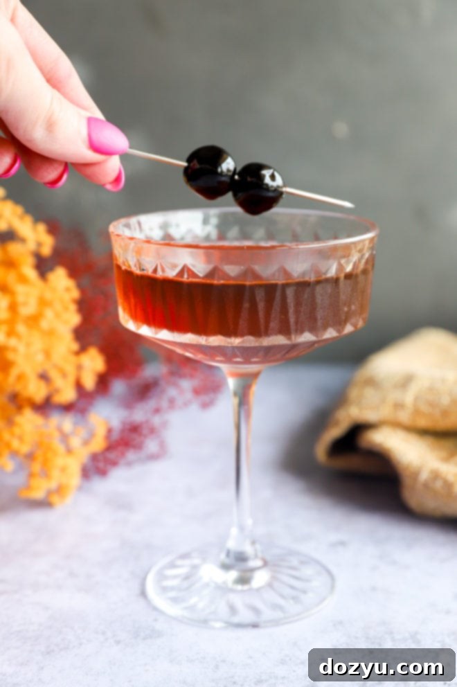 Bourbon Manhattan A Timeless Classic 2 Adding a cherry garnish to a coupe glass filled with a Bourbon Manhattan cocktail