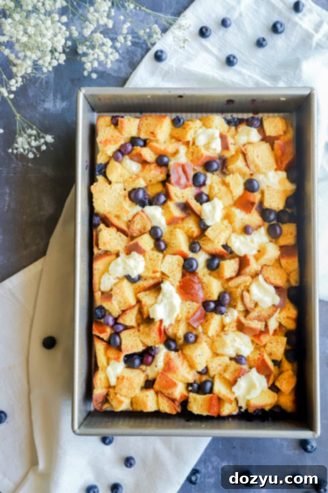 Blueberry & Cream Cheese French Toast Bake 5 Overhead view of an unbaked overnight French toast casserole in a baking pan, showing layers of bread, cream cheese, and blueberries before soaking.