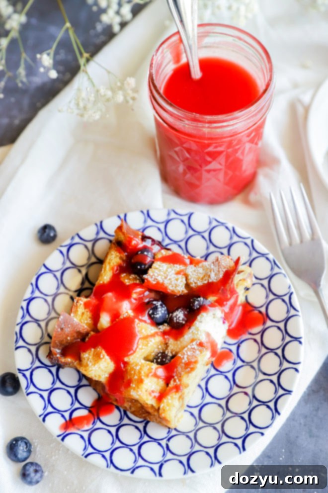 Blueberry & Cream Cheese French Toast Bake 7 A slice of Blueberry Cream Cheese French Toast Casserole showcasing its red, white, and blue colors, topped with fruit.