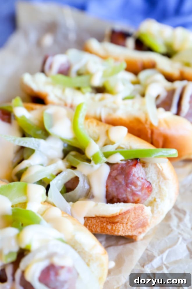 Philly Cheesesteak Beer Brats 3 Grilled bratwursts lined up on buns, generously topped with beer-braised onions and peppers and drizzled with a rich cheese sauce.