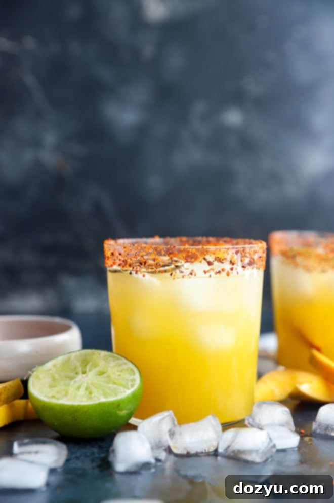 Spicy Mango Margarita Two spicy mango cocktails garnished with jalapeño and lime slices, set against a vibrant background.