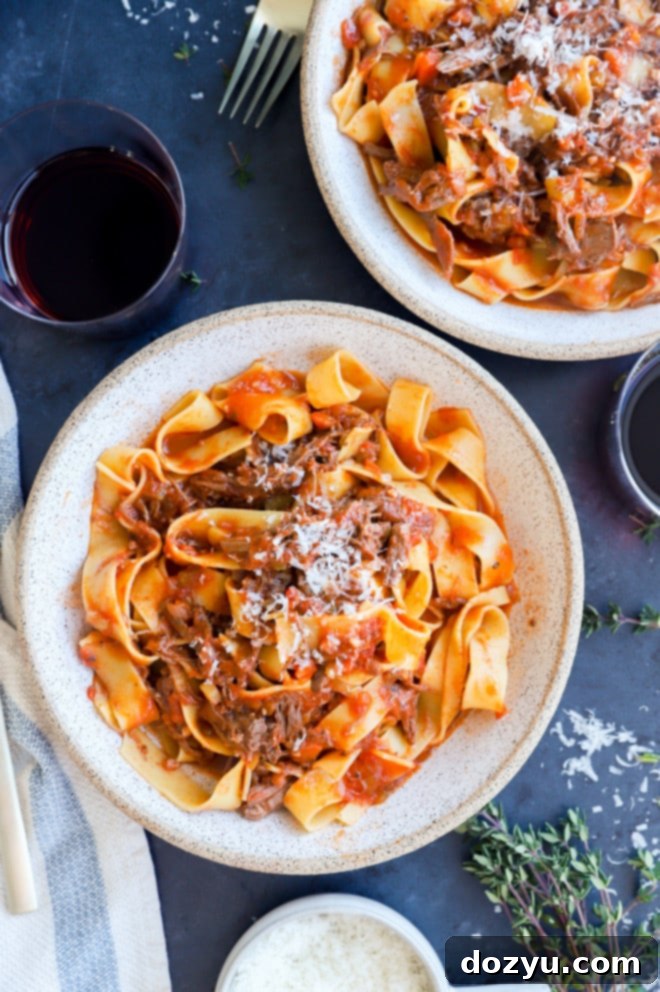 Fall-Off-The-Bone Instant Pot Short Rib Ragu 12 A bowl of Instant Pot Short Rib Ragu with wide pasta, fresh parsley, and a piece of crusty bread on the side.