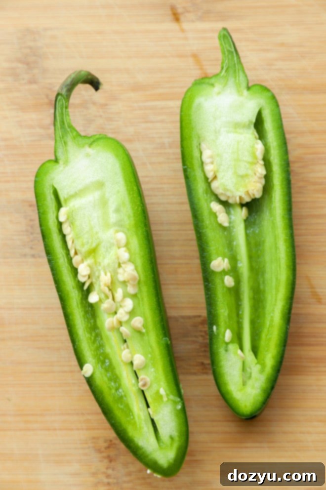 Master Jalapeno Seeding 4 Two whole jalapeños next to two halved jalapeños, showing how they look before preparation for dishes like poppers