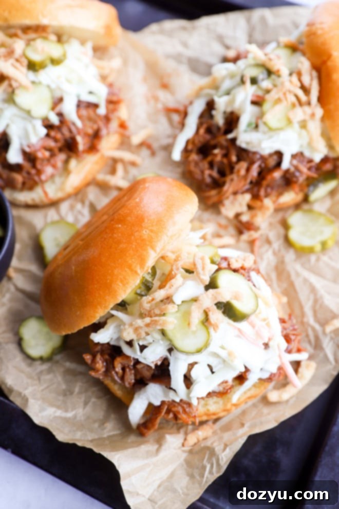 Two perfectly arranged pulled pork burgers on parchment paper, set on a sheet pan, ready to be served.