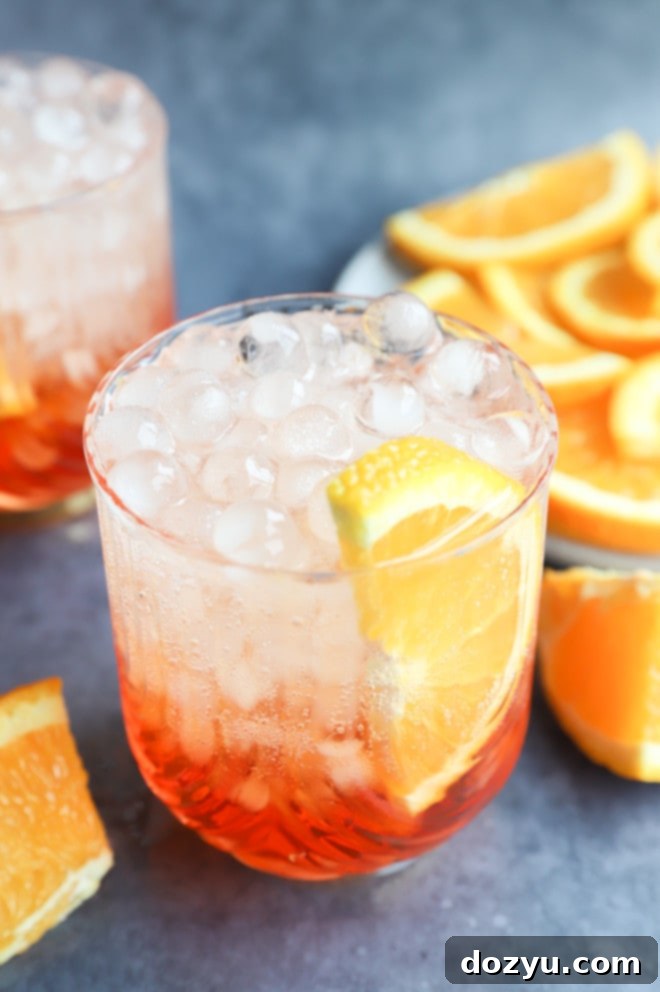 Aperol Fizz 8 Close-up of a single Aperol Soda cocktail in an elegant glass with ice and a fresh orange slice, showcasing its vibrant color.