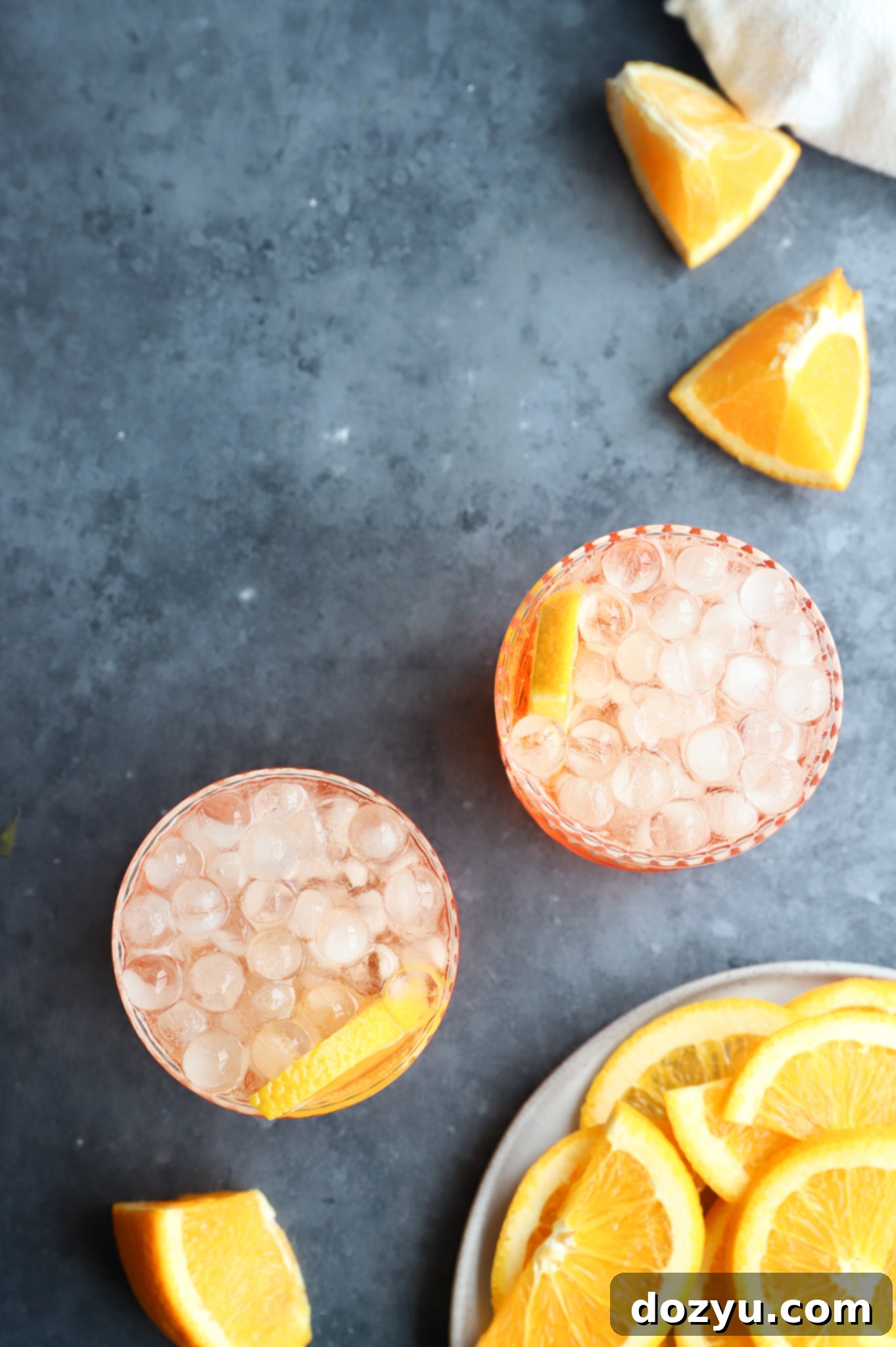 Aperol Fizz 6 Overhead view of two Aperol Soda cocktails in elegant glasses, garnished with orange slices, on a light background.