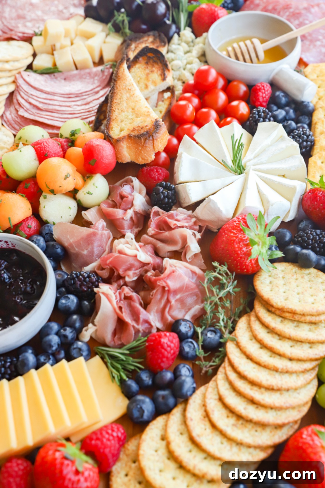Effortless Summer Grazing Board 3 Close-up picture of brie, fresh herbs, colorful fruits, and cured meats on a charcuterie board
