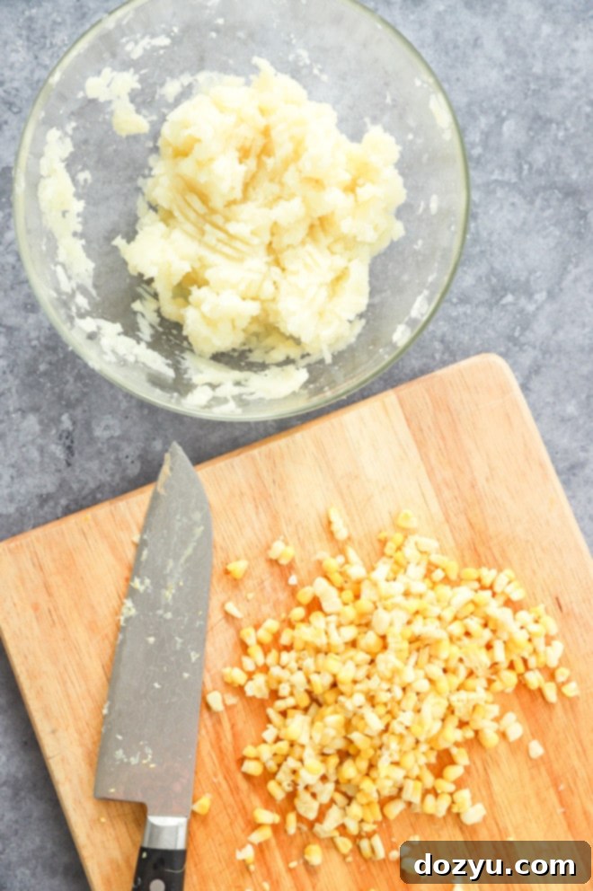 Cheesy Corn Bites 4 Mashed potato in a white bowl with fresh corn kernels scattered on a wooden cutting board beside it.