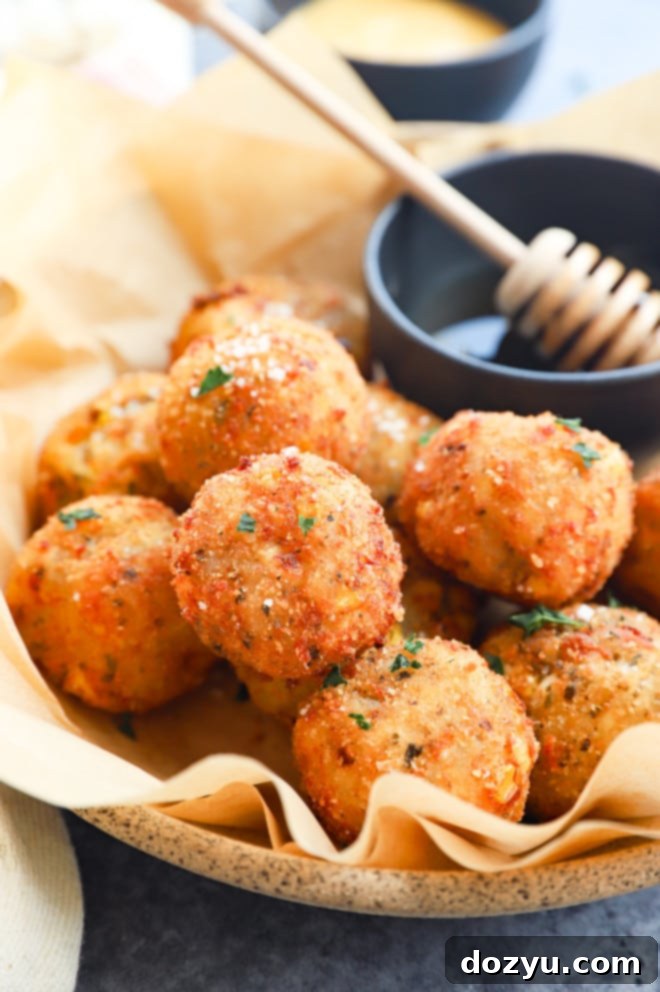 Cheesy Corn Bites 8 Close-up of golden-brown fried cheese corn balls drizzled with honey in a white bowl.