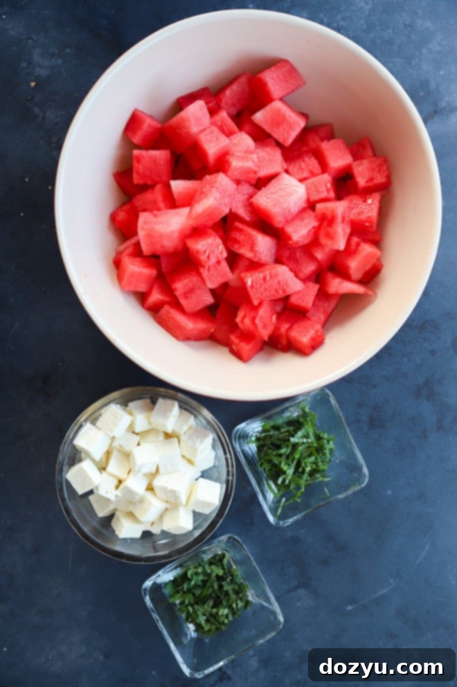 Refreshing Watermelon Feta Delight 3 Close-up shot of fresh ingredients for Watermelon Feta Salad, including neatly cubed watermelon, a block of feta cheese, and bunches of fresh basil and mint.