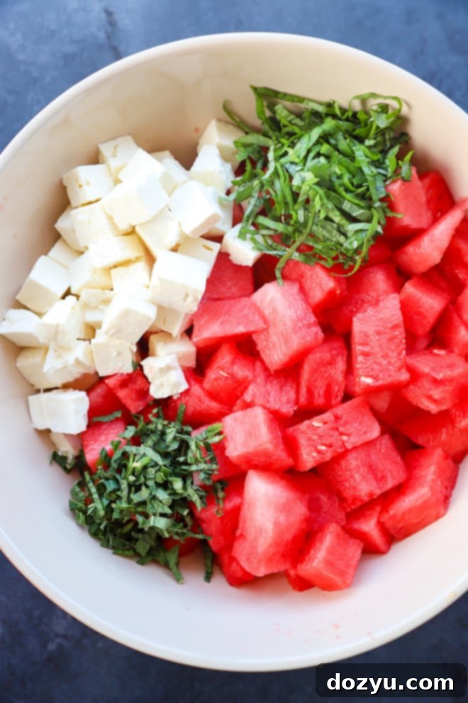 Refreshing Watermelon Feta Delight 4 Hands gently tossing cubed watermelon, feta cheese, and fresh herbs in a large mixing bowl with a light dressing, illustrating the preparation process.