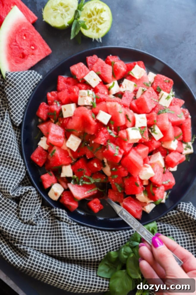 Refreshing Watermelon Feta Delight 8 A hand holding a serving spoon, scooping a portion of fresh Watermelon Feta Salad from a large platter, ready to be served.